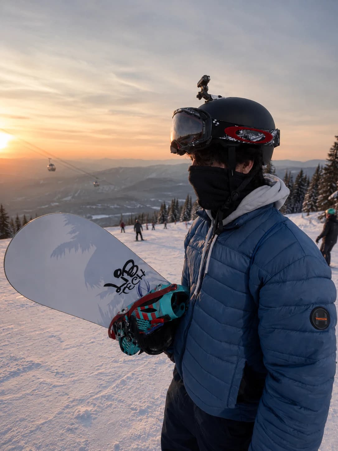 Snowboarder holding a LibTech board on a mountain at sunset
